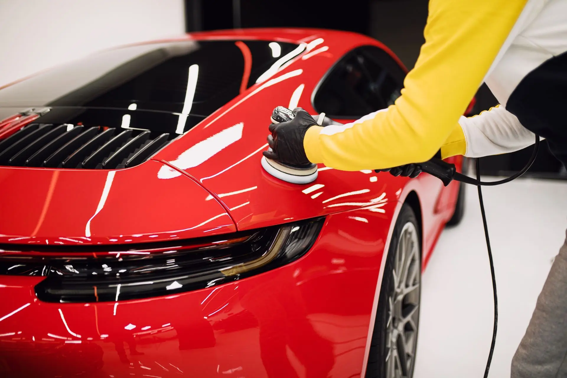 A Duluth Detail technician machine-polishing the fender of a red car in a driveway
